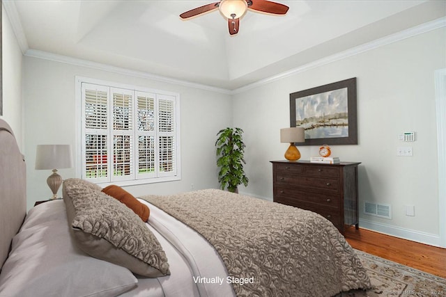 bedroom with wood-type flooring, a raised ceiling, ceiling fan, and crown molding