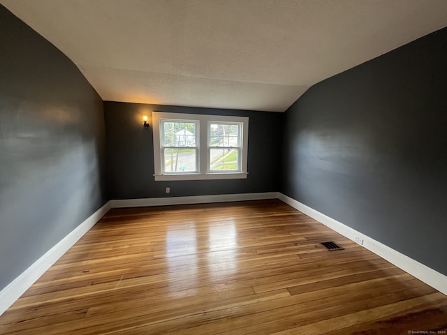 empty room featuring light wood-type flooring, a textured ceiling, and lofted ceiling