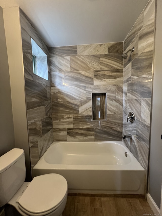 bathroom with tiled shower / bath combo, toilet, and wood-type flooring