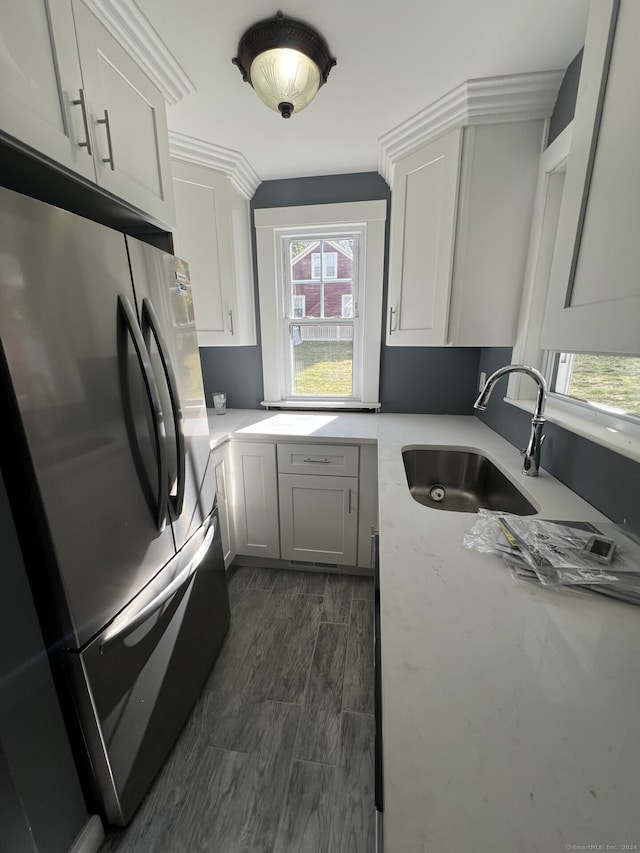 kitchen with ornamental molding, stainless steel fridge, sink, and white cabinetry