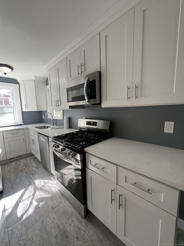 kitchen featuring stainless steel appliances, white cabinetry, light stone counters, and sink