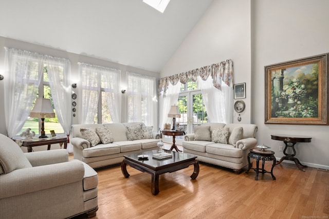 living room featuring high vaulted ceiling, light hardwood / wood-style flooring, a skylight, and plenty of natural light