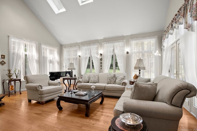 living room with light hardwood / wood-style flooring, a skylight, and high vaulted ceiling