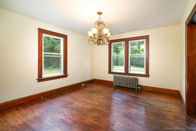 spare room featuring dark wood-type flooring, radiator heating unit, and a chandelier