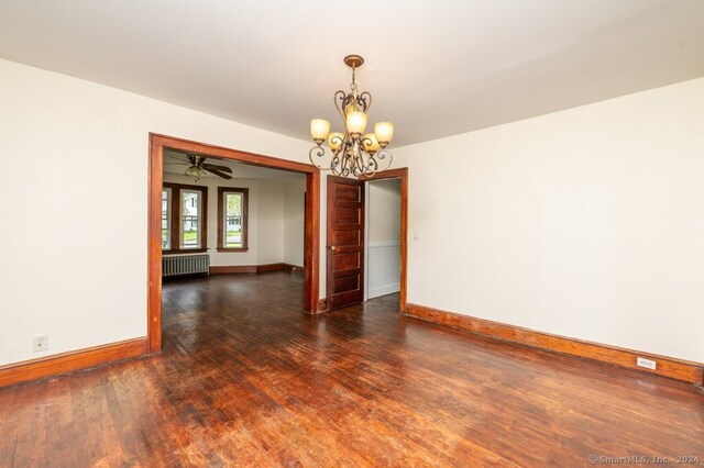 unfurnished room with ceiling fan with notable chandelier, dark hardwood / wood-style flooring, and radiator heating unit