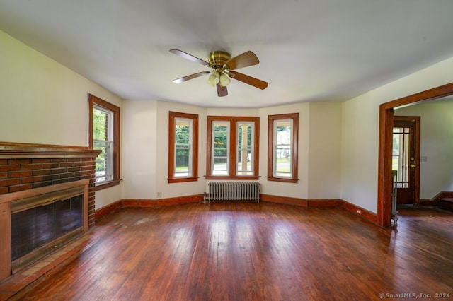 unfurnished living room with a brick fireplace, radiator, dark hardwood / wood-style flooring, and ceiling fan