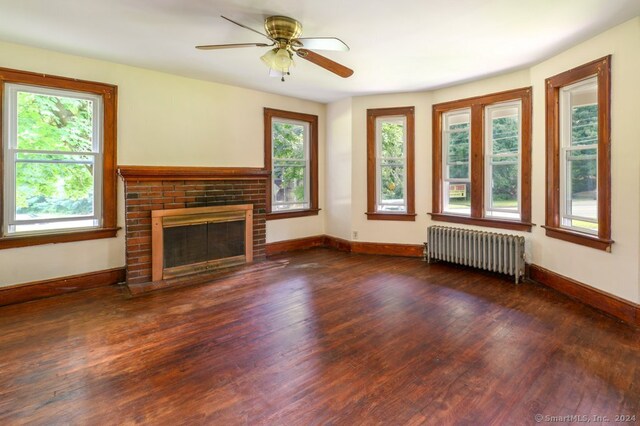 unfurnished living room with radiator heating unit, dark wood-type flooring, ceiling fan, and a fireplace