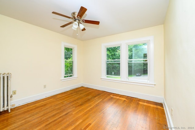 empty room featuring ceiling fan, hardwood / wood-style floors, and radiator heating unit