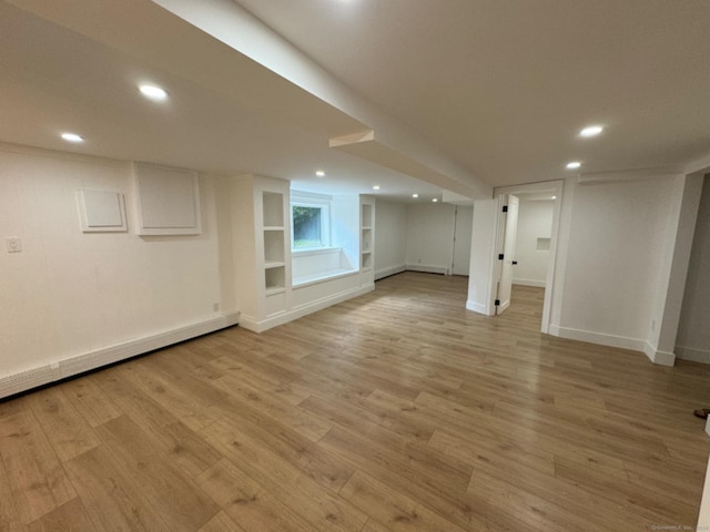 basement featuring built in features, a baseboard radiator, and light hardwood / wood-style flooring