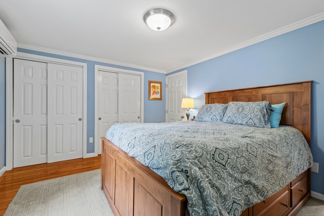 bedroom featuring ornamental molding, light wood-type flooring, two closets, and a wall mounted AC