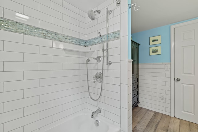 bathroom with wood-type flooring, tiled shower / bath combo, and tile walls