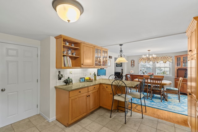 kitchen with light stone counters, hanging light fixtures, backsplash, an inviting chandelier, and light wood-type flooring