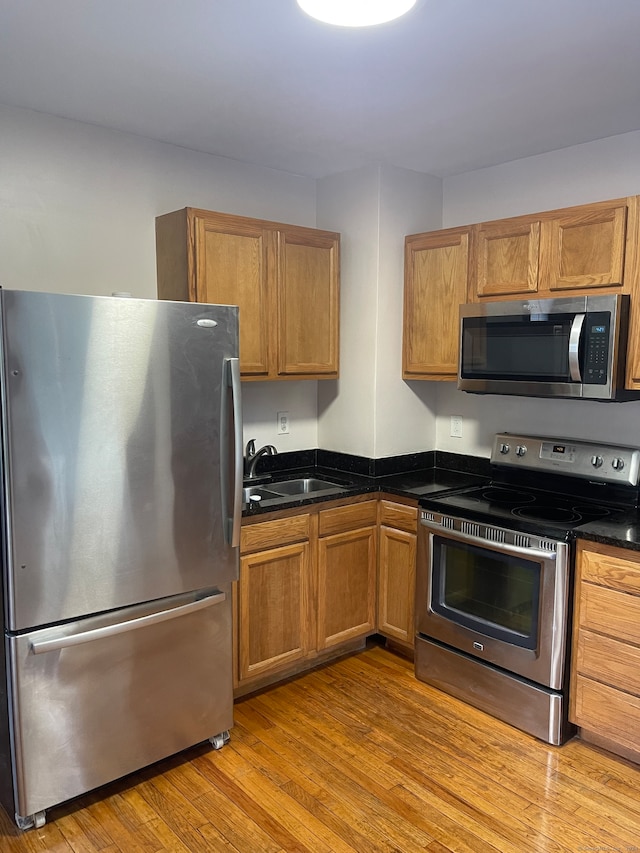 kitchen with light hardwood / wood-style flooring, appliances with stainless steel finishes, sink, and dark stone counters