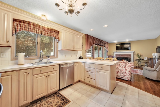 kitchen featuring light wood-type flooring, kitchen peninsula, stainless steel dishwasher, an inviting chandelier, and a fireplace