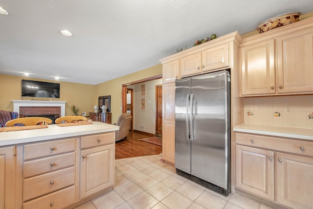 kitchen featuring stainless steel fridge, tasteful backsplash, a textured ceiling, light hardwood / wood-style flooring, and a fireplace