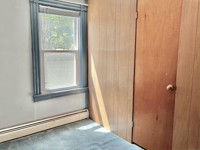 unfurnished bedroom with a baseboard radiator, wooden walls, and carpet