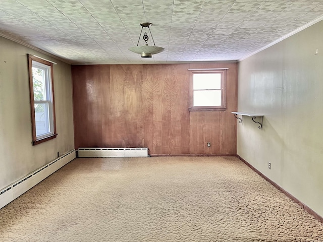 spare room featuring baseboard heating, wood walls, carpet flooring, and crown molding