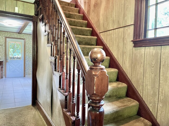 stairway with wood walls and tile patterned floors