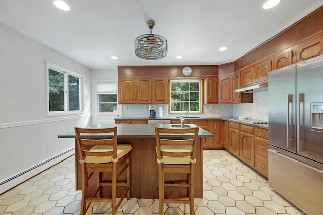 kitchen with decorative backsplash, a breakfast bar, a kitchen island, stainless steel appliances, and a baseboard heating unit