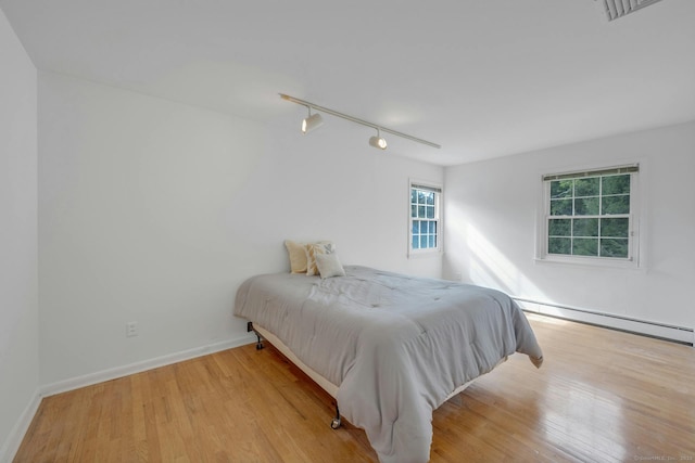 bedroom with track lighting, light hardwood / wood-style flooring, and a baseboard radiator