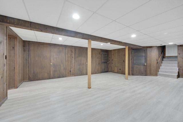 basement featuring light hardwood / wood-style flooring, wood walls, and a drop ceiling