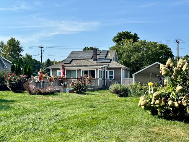 rear view of house featuring a lawn, a deck, and solar panels