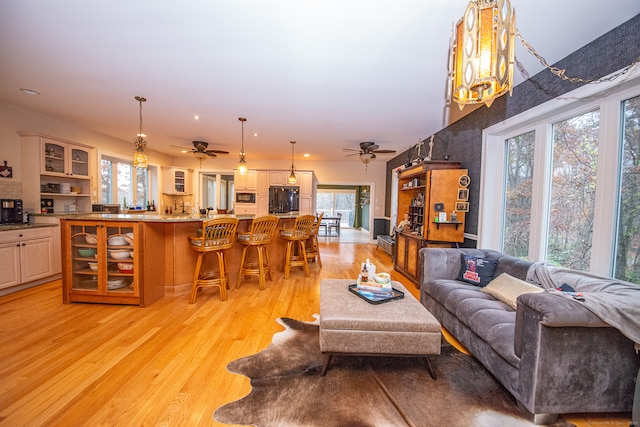 living room featuring light hardwood / wood-style floors, plenty of natural light, and ceiling fan with notable chandelier