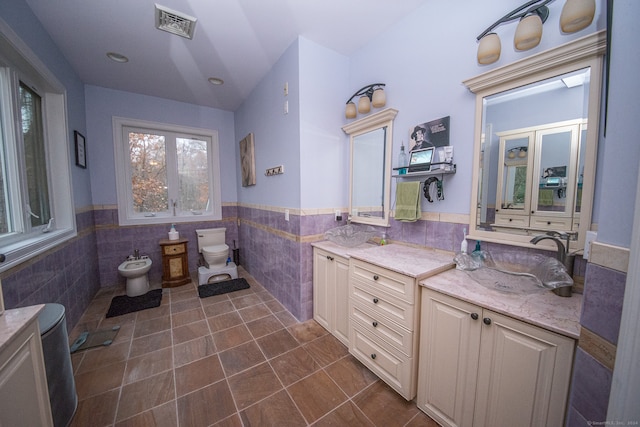 bathroom with vanity, tile walls, a bidet, and toilet