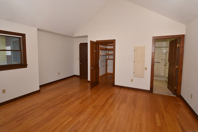 unfurnished bedroom featuring connected bathroom, high vaulted ceiling, and light hardwood / wood-style flooring