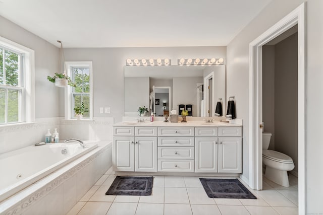 bathroom with tiled tub, vanity, tile patterned flooring, and toilet