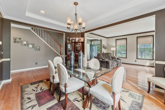 dining space with a notable chandelier, light wood-type flooring, a tray ceiling, and crown molding