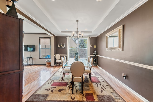 dining area with a notable chandelier, light hardwood / wood-style flooring, crown molding, and a tray ceiling