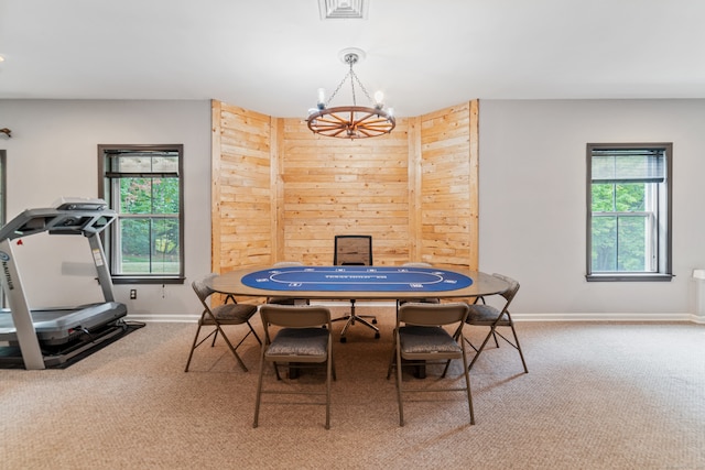 carpeted dining space featuring a chandelier, wood walls, and a healthy amount of sunlight