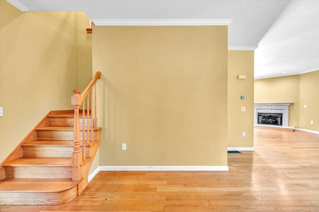 stairway with a fireplace, ornamental molding, and hardwood / wood-style flooring