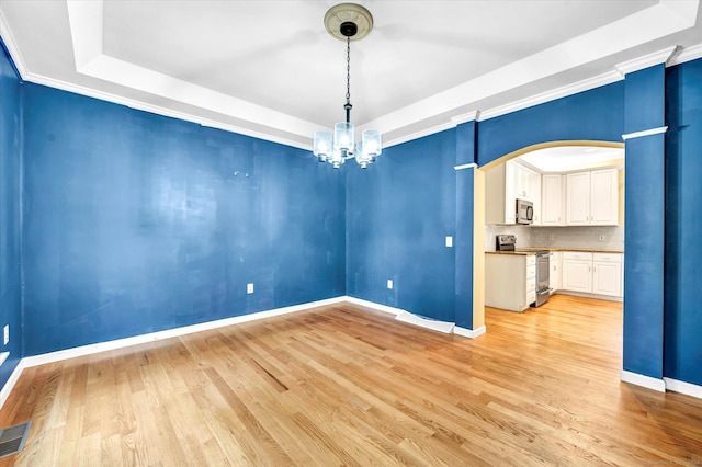 unfurnished dining area with ornamental molding, an inviting chandelier, light hardwood / wood-style flooring, and a raised ceiling