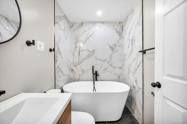 bathroom featuring vanity, a tub to relax in, toilet, and tile walls