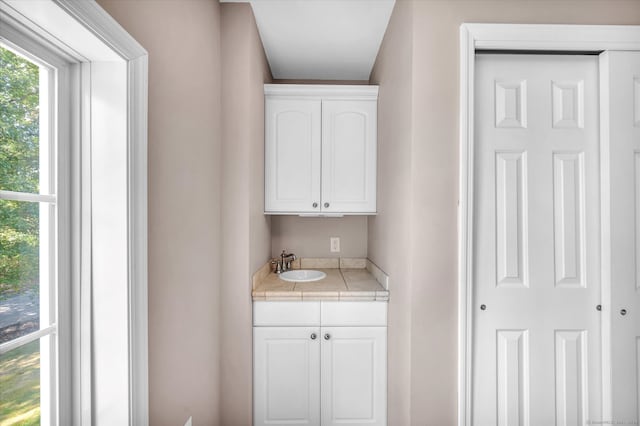 bar with white cabinets, tile countertops, and sink