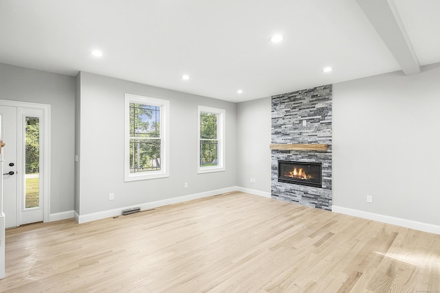 unfurnished living room featuring a fireplace, beam ceiling, and light hardwood / wood-style floors