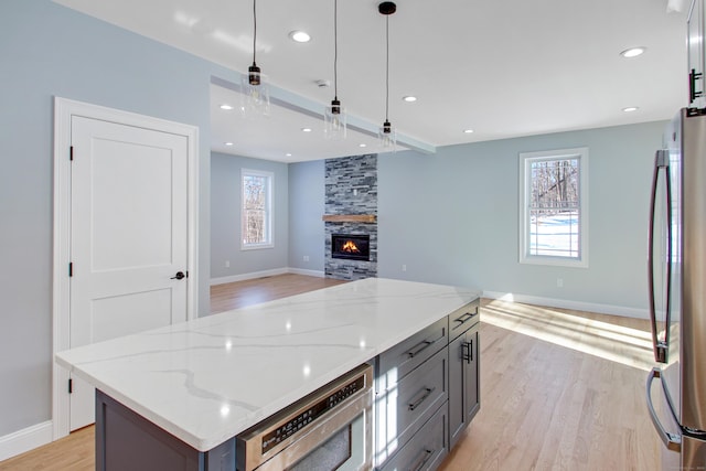 kitchen featuring hanging light fixtures, a kitchen island, light stone countertops, and stainless steel fridge