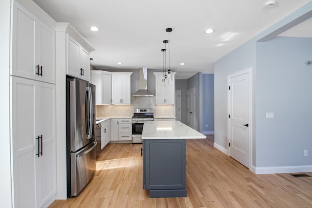 kitchen featuring white cabinetry, hanging light fixtures, a kitchen island, stainless steel appliances, and wall chimney range hood