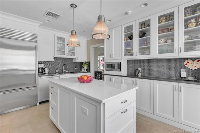 kitchen featuring built in appliances, hanging light fixtures, tasteful backsplash, and white cabinetry