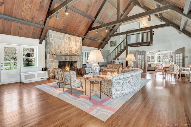 living room featuring high vaulted ceiling, hardwood / wood-style flooring, and a stone fireplace