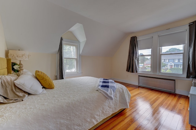 bedroom featuring radiator heating unit, vaulted ceiling, multiple windows, and light hardwood / wood-style flooring