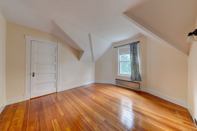 bonus room with light wood-type flooring, vaulted ceiling, and radiator heating unit