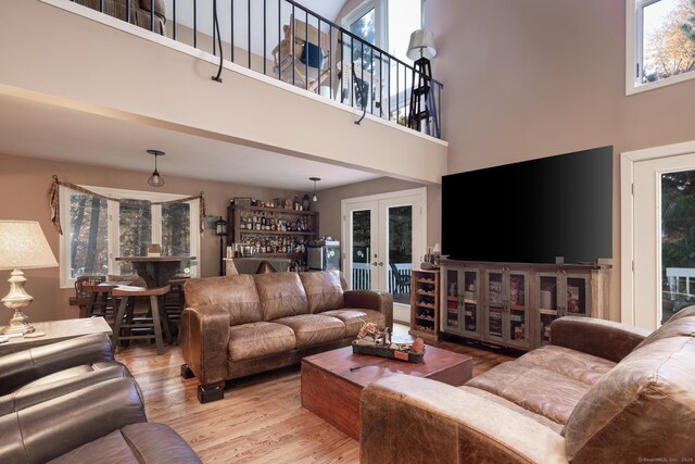 living room with light hardwood / wood-style floors, a towering ceiling, and french doors