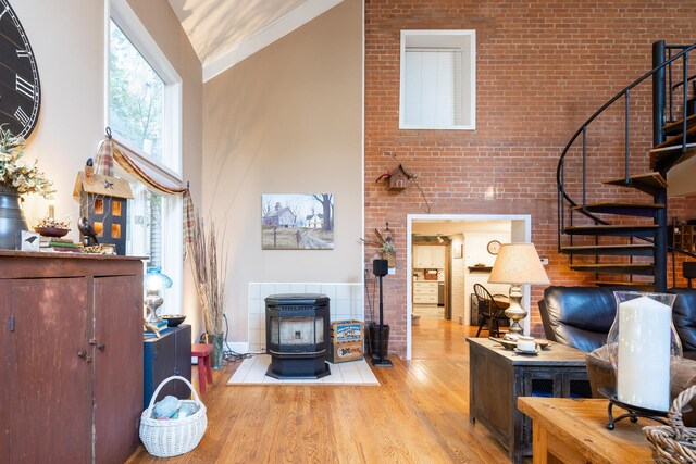 home office featuring a high ceiling, a wood stove, light wood-type flooring, and brick wall