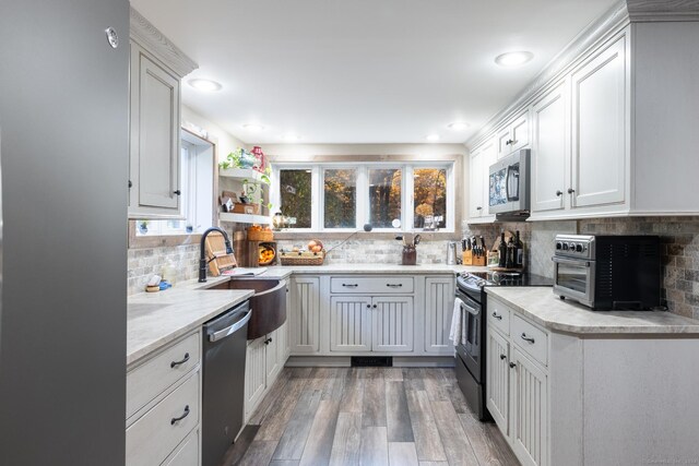 kitchen with hardwood / wood-style floors, sink, decorative backsplash, white cabinetry, and stainless steel appliances