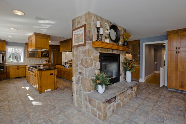 kitchen featuring stainless steel gas stovetop, a stone fireplace, tasteful backsplash, and a kitchen island