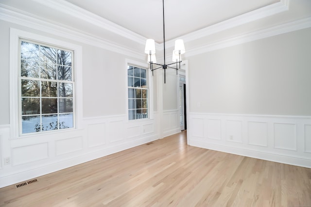 unfurnished dining area featuring a chandelier, light hardwood / wood-style floors, a tray ceiling, and crown molding