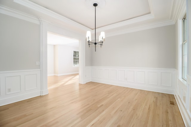 unfurnished dining area featuring a notable chandelier, light hardwood / wood-style floors, ornamental molding, and a tray ceiling